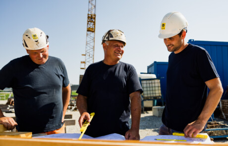 2 Poliere und 1 Bauleiter besprechen einen Bauplan auf der Baustelle