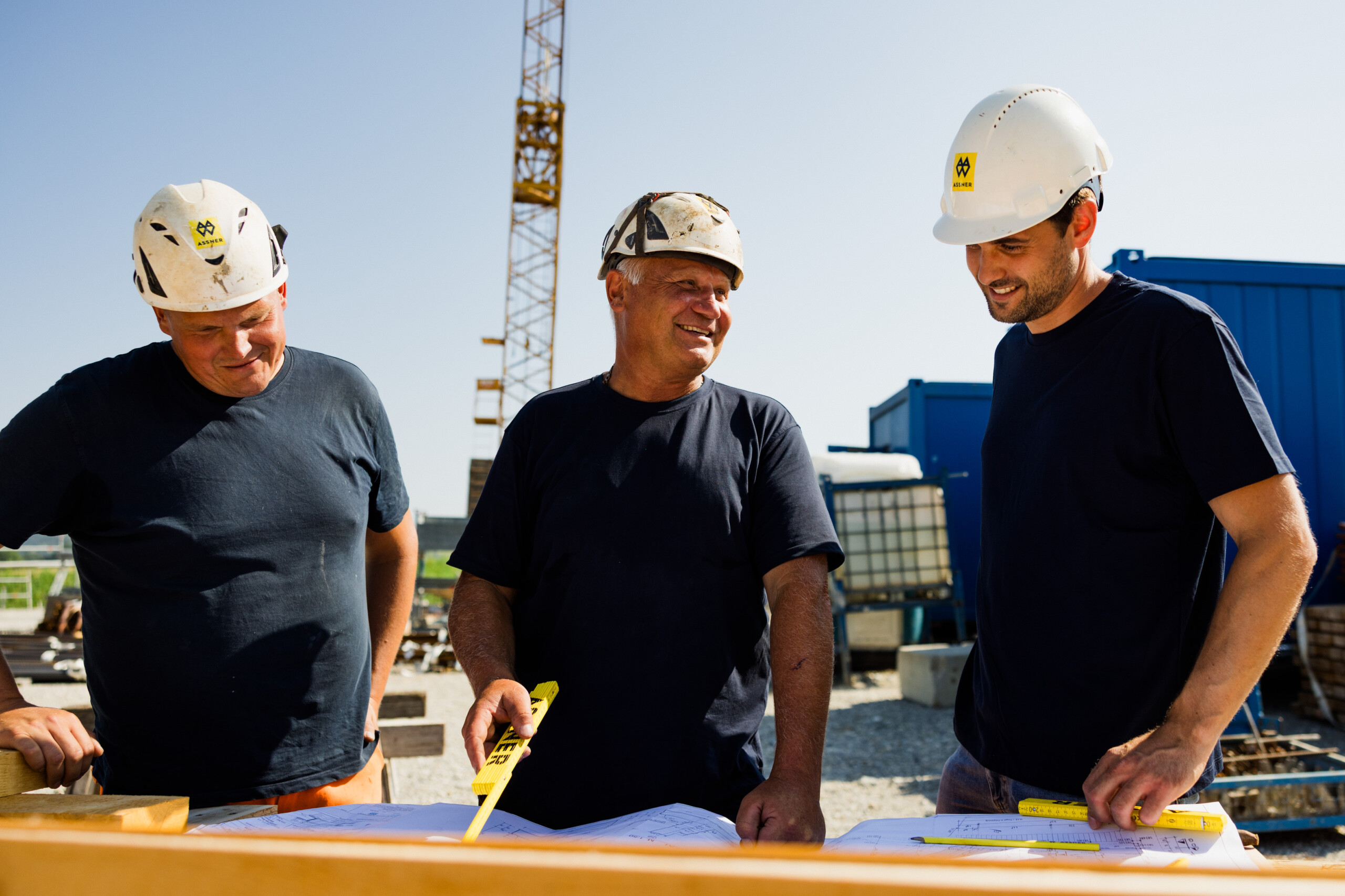 2 Poliere und 1 Bauleiter besprechen einen Bauplan auf der Baustelle